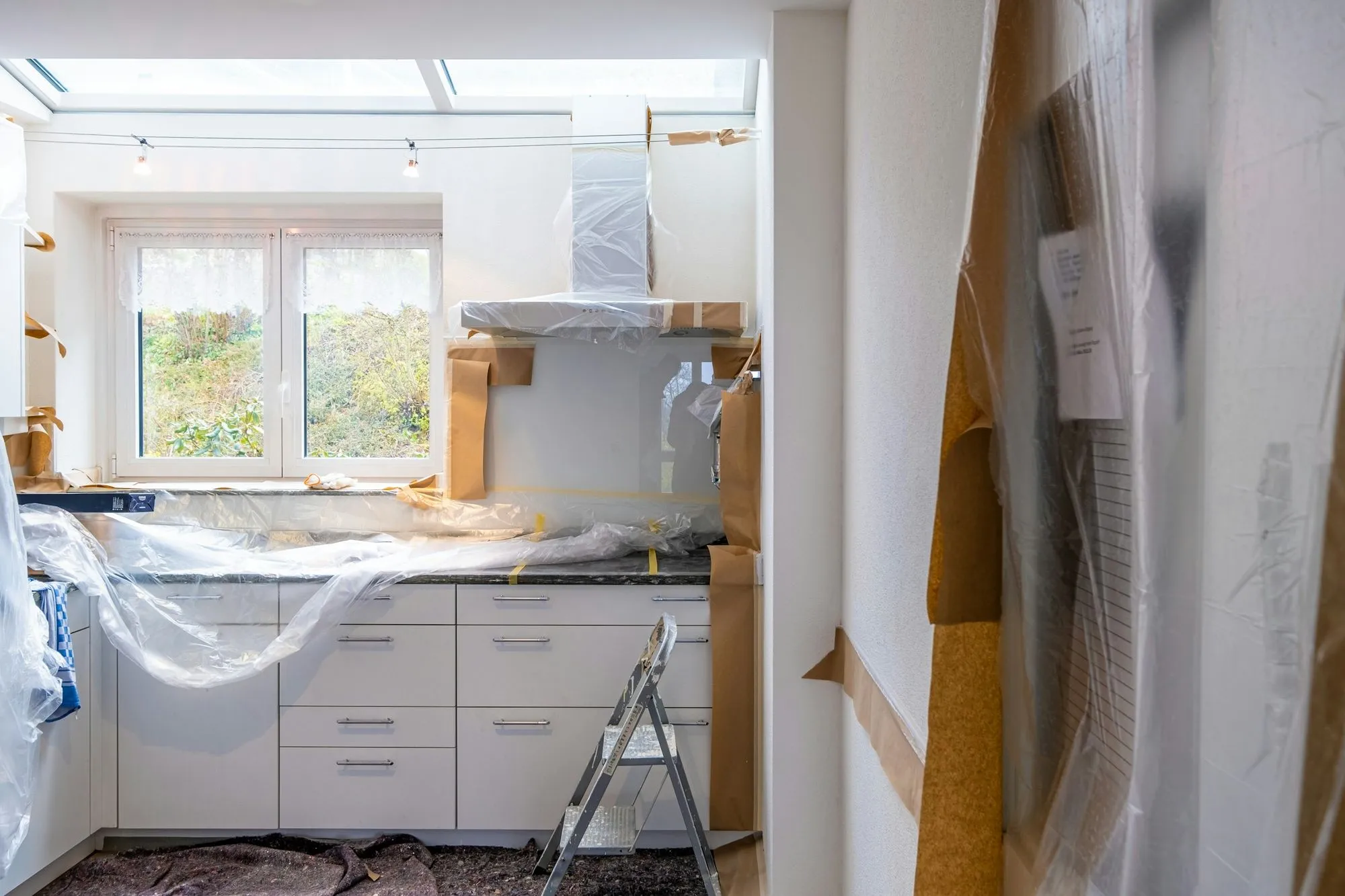 Kitchen mid-renovation with new white cabinets wrapped in plastic and the floor covered in paper