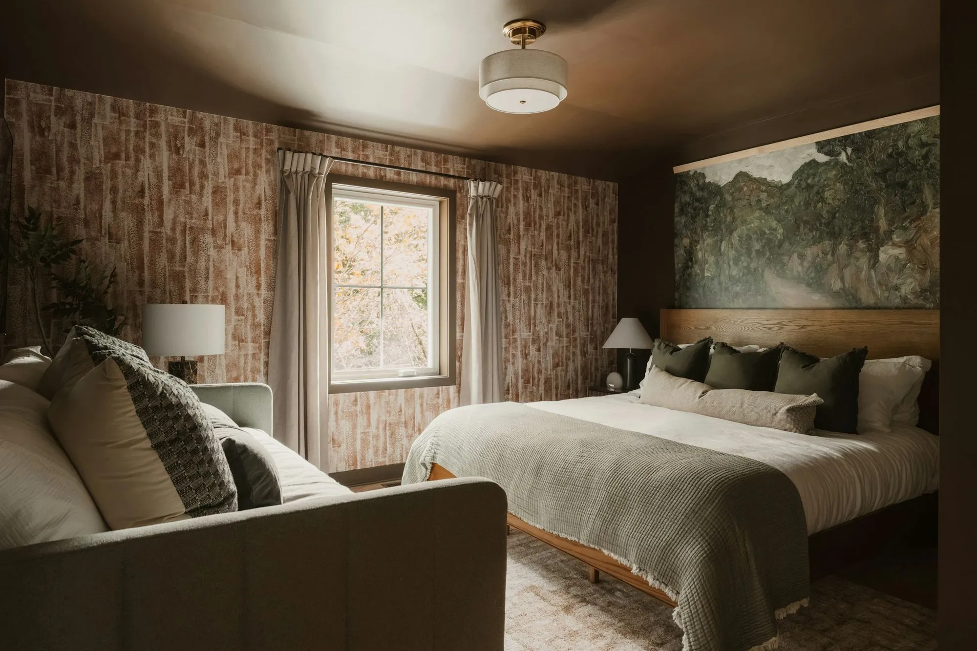 Bedroom with textured wallpaper, a landscape mural over the bed and a sofa at its foot