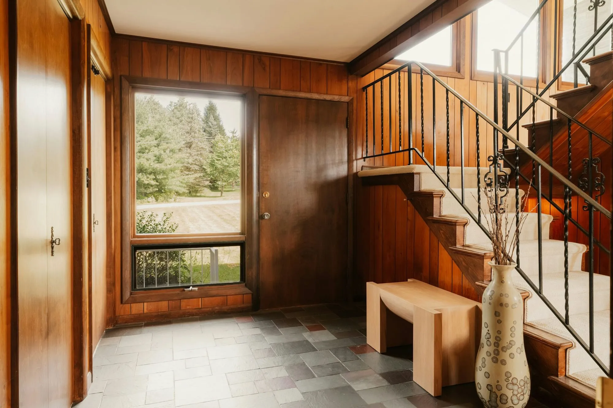 Entry hall with walnut paneling, a slate floor, an open stair with iron railings and a tall window
