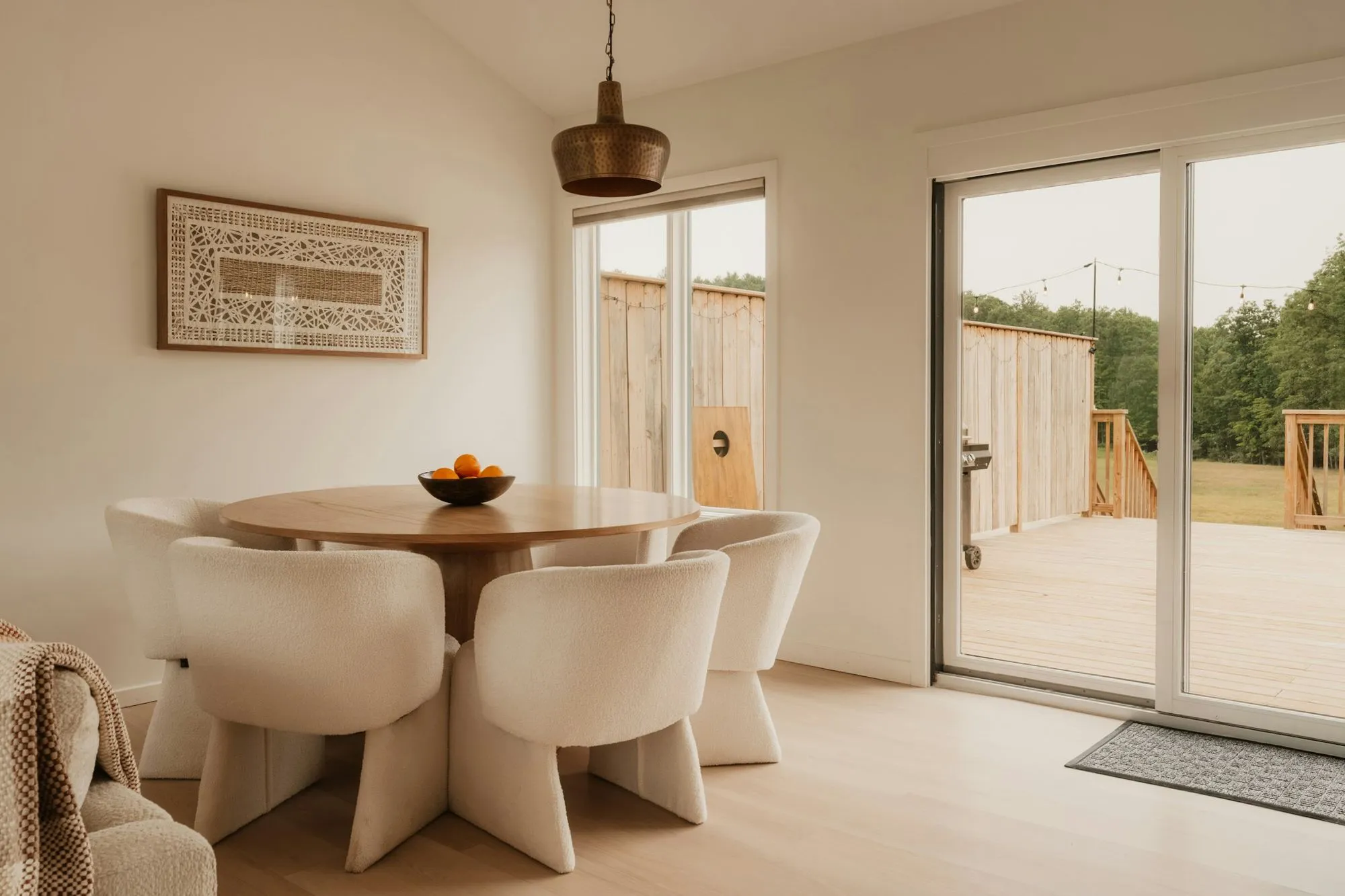 Round dining table with four white upholstered chairs beside sliding doors to a deck