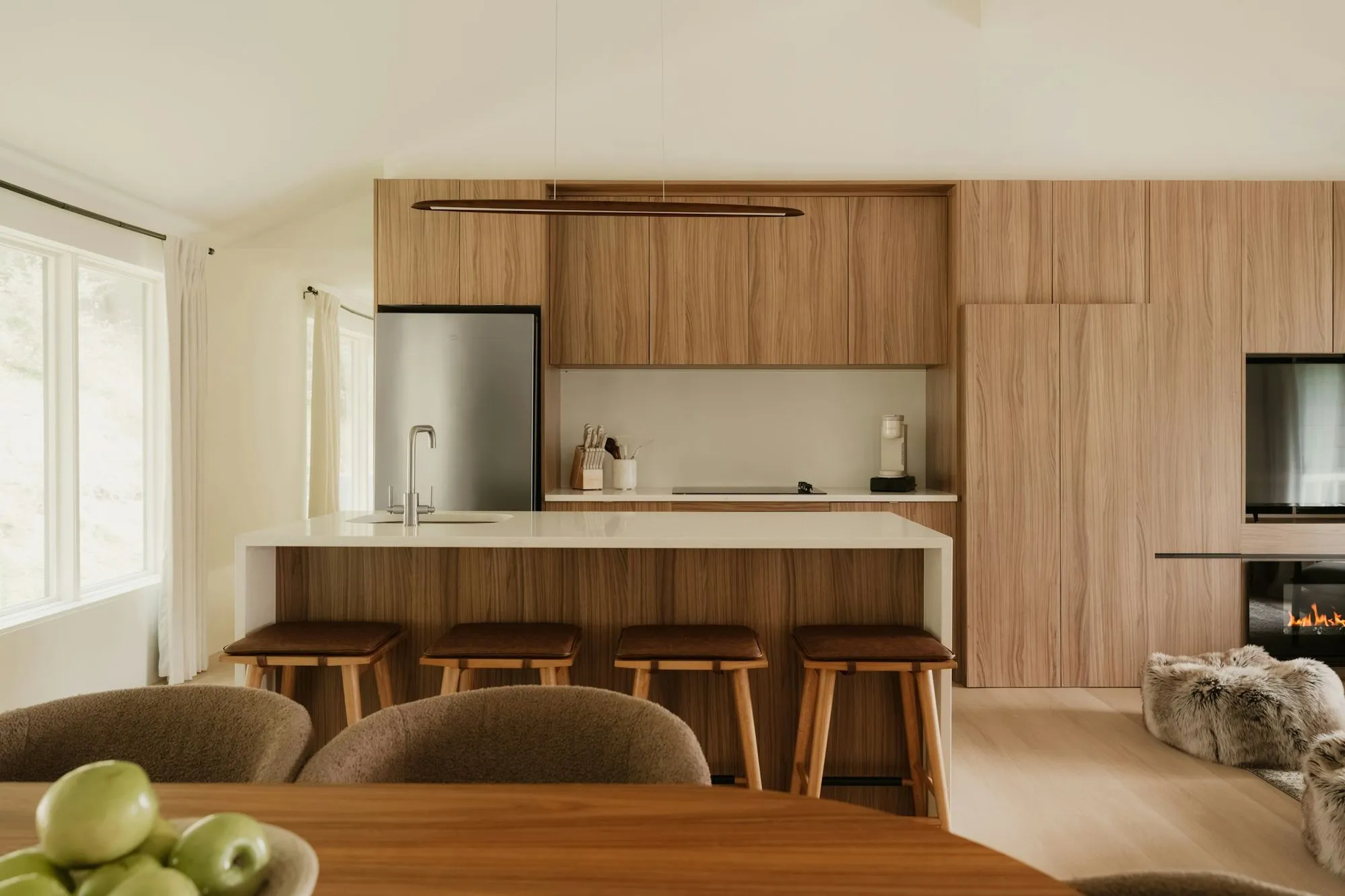 Kitchen with a wall of walnut cabinets, a white island with four wood stools and a dining table in front